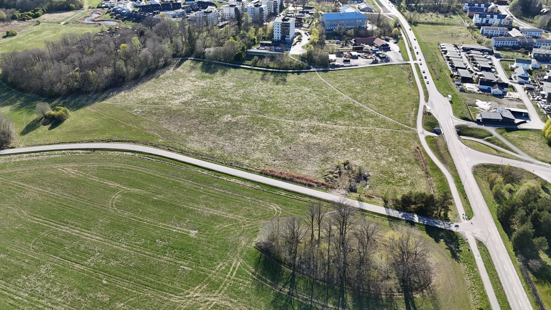 Drönarvy från öster över Tälje 3:188 — öppen jordbruksmark omgiven av åkrar, skog och bostadsbebyggelse.